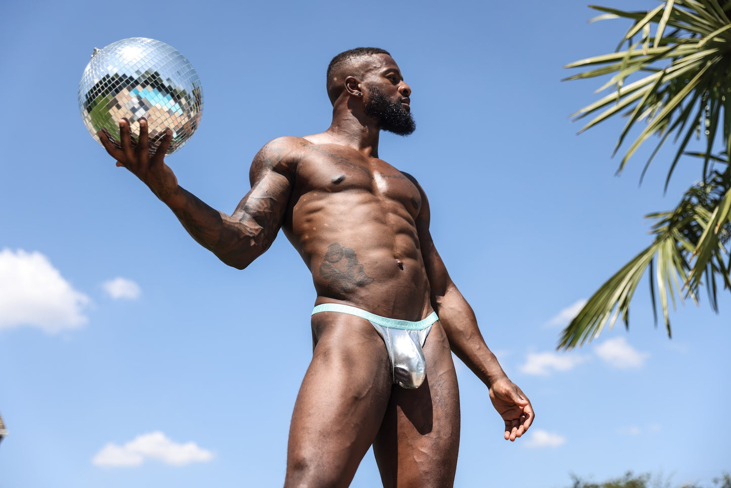 Man posing in silver thong underwear holding a disco ball